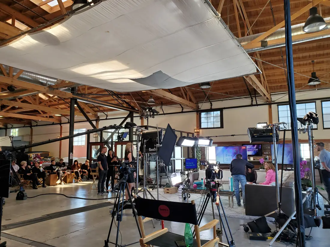A talk-show set under a large silk diffusion frame inside a timber-beam studio, with a camera on a tripod.