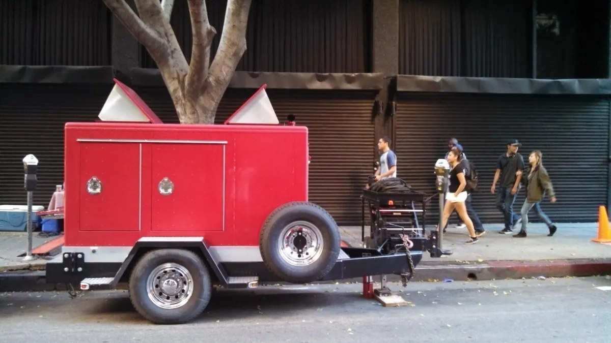 A red motion-picture generator trailer and power distribution staged along a downtown city street during a shoot.