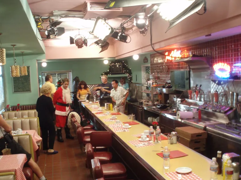 A retro diner interior dressed and lit for a shoot, with film fixtures rigged to the ceiling over the counter.